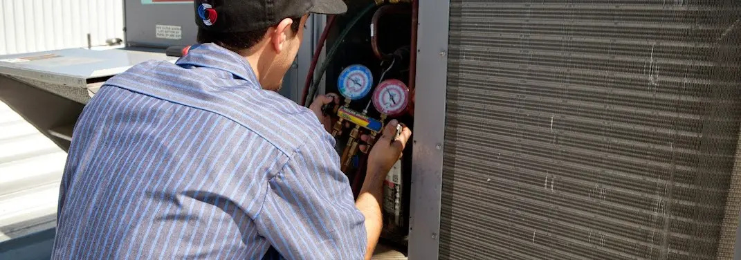 HVAC technician servicing a condenser unit in Bolton
